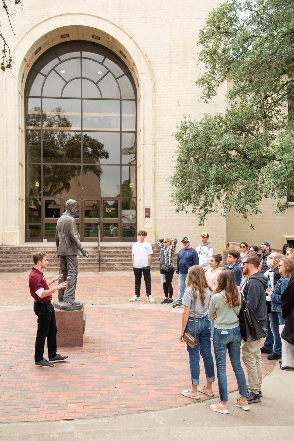 A tour guide talking to a group of visitors near the LBJ statue on campus.
