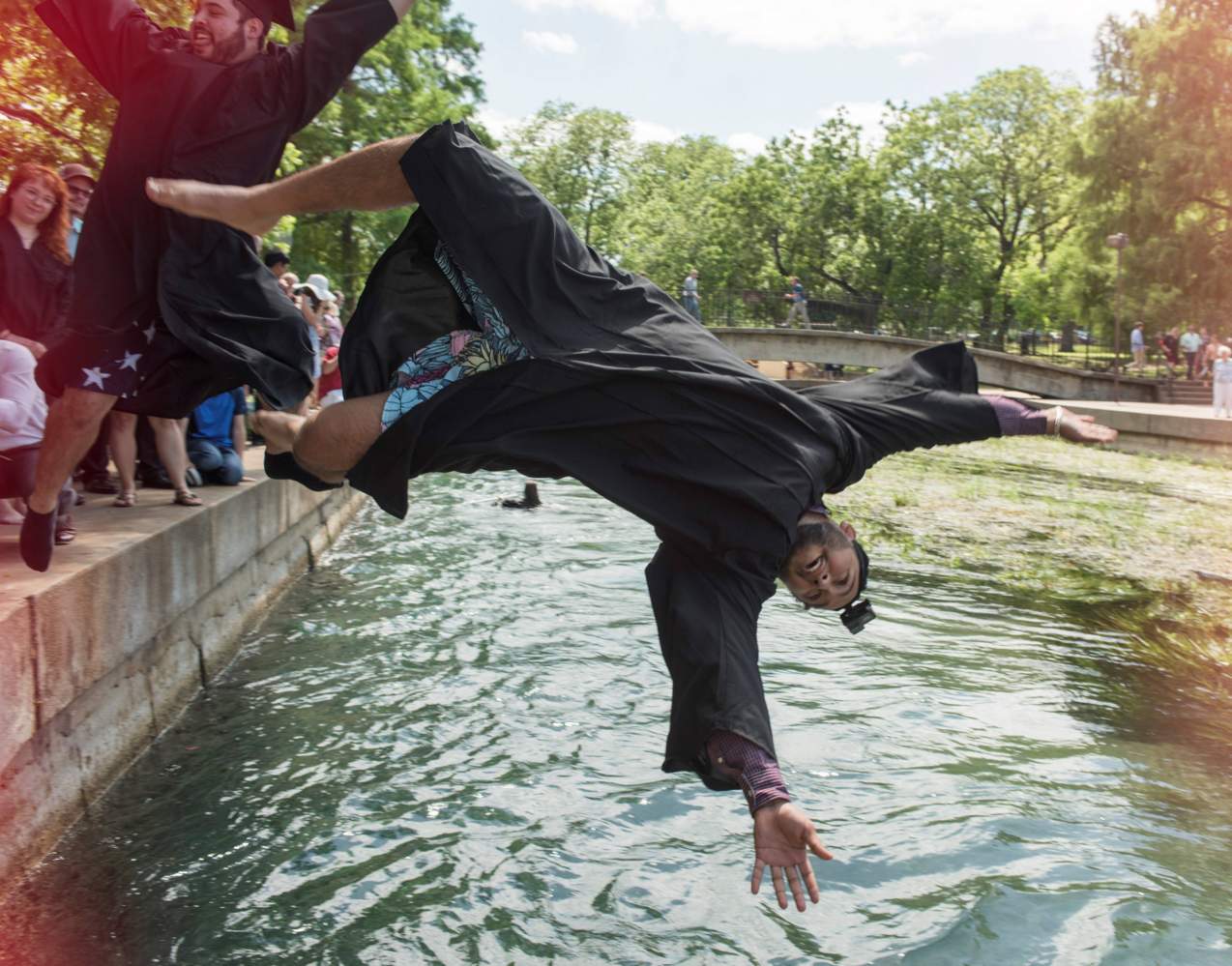 student jumping into san marcos river in cap and gown