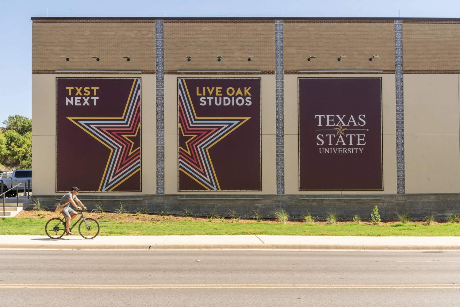 Three big banners hanging on a new building feature TXST branding and brightly colored line art of a star over a field of maroon.