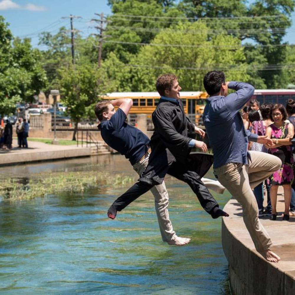 three graduates jump backwards into the river