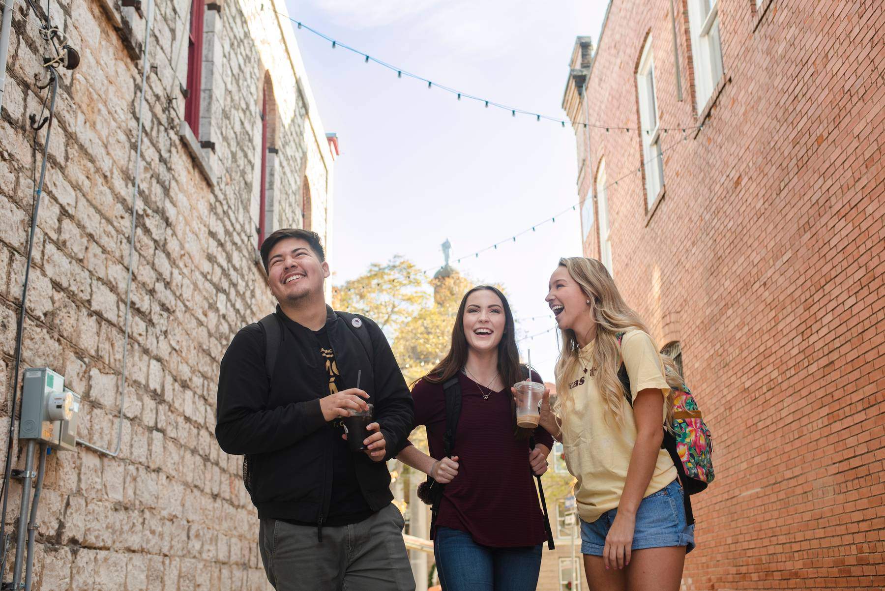 Three students in an alley between two brick buildings.