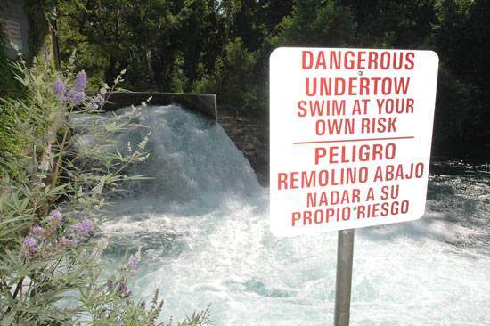 Sign in front of the falls in San Marcos River warning of danger