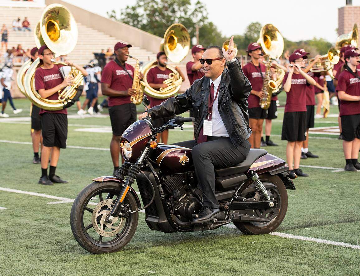 President Damphousse riding a motorcycle on the football field