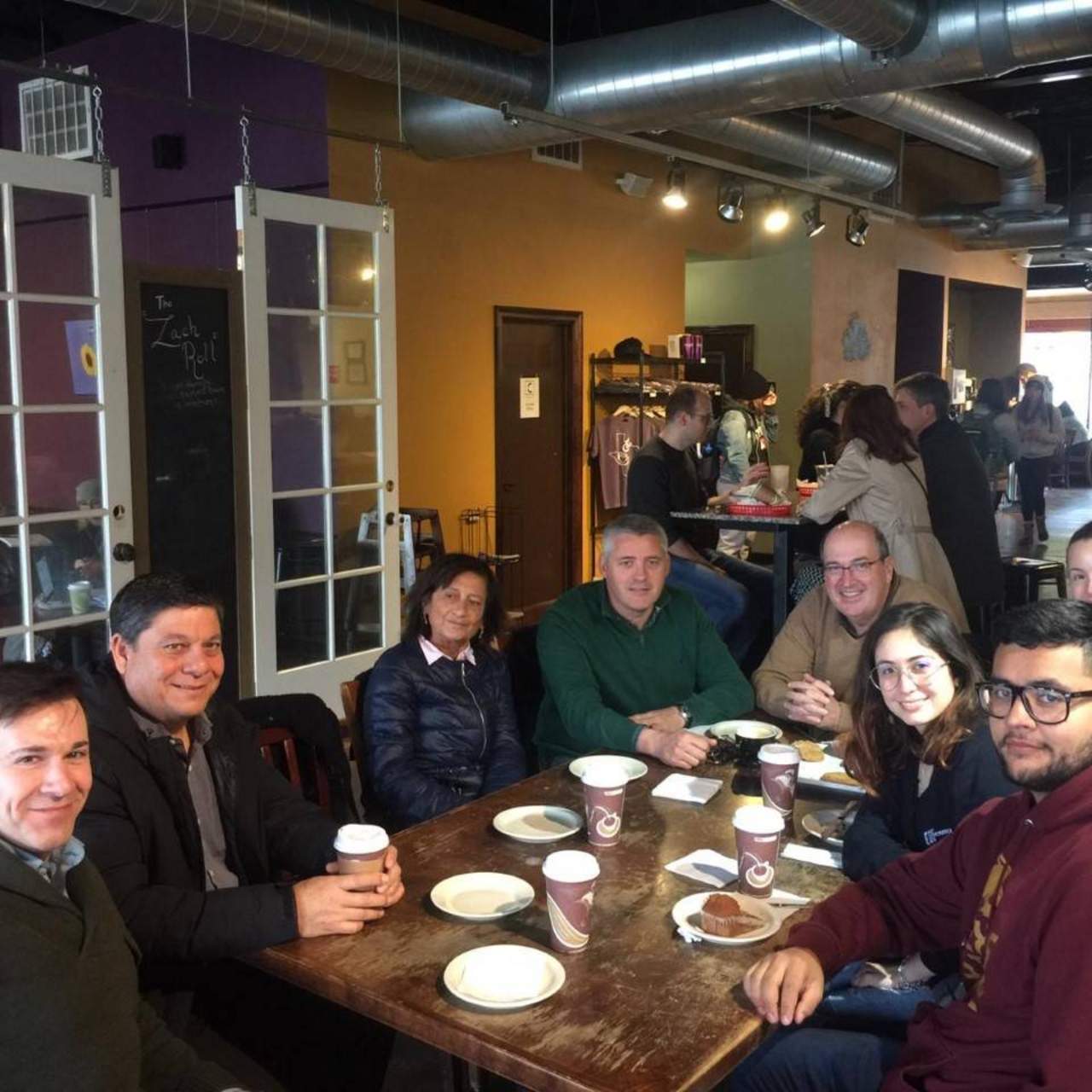 Students and members of Spanish delegation sitting at a table in a coffee shop, taken from a different angle