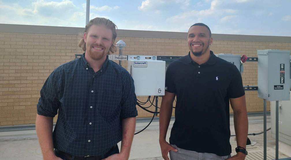 two men standing next to antenna on rooftop