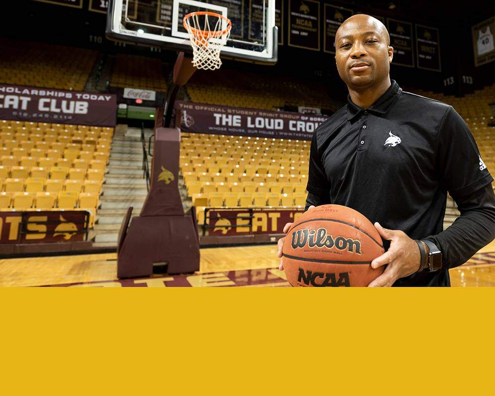 Basketball coach stands in front of yellow cour and seats with stripe of yellow color