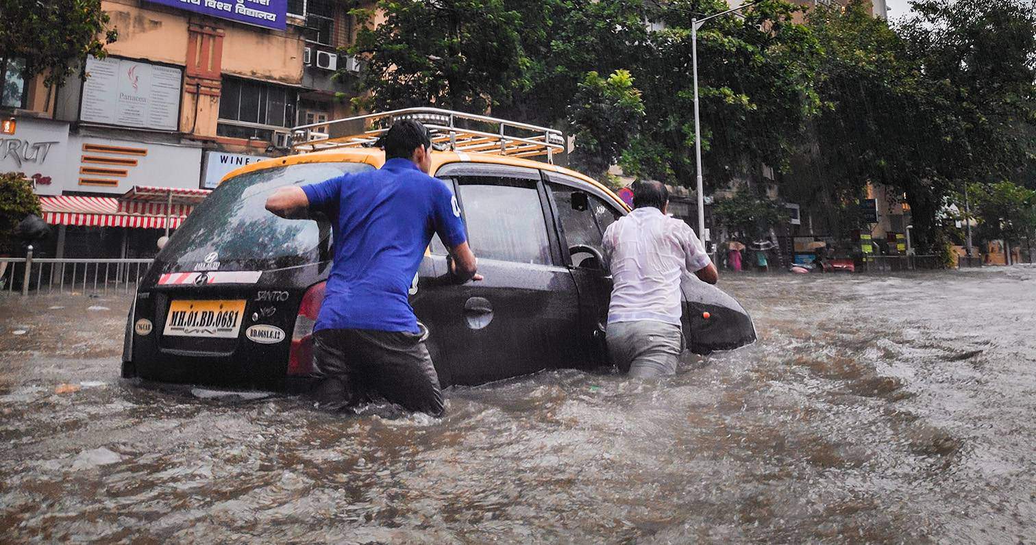 two people pushing car through flooded street