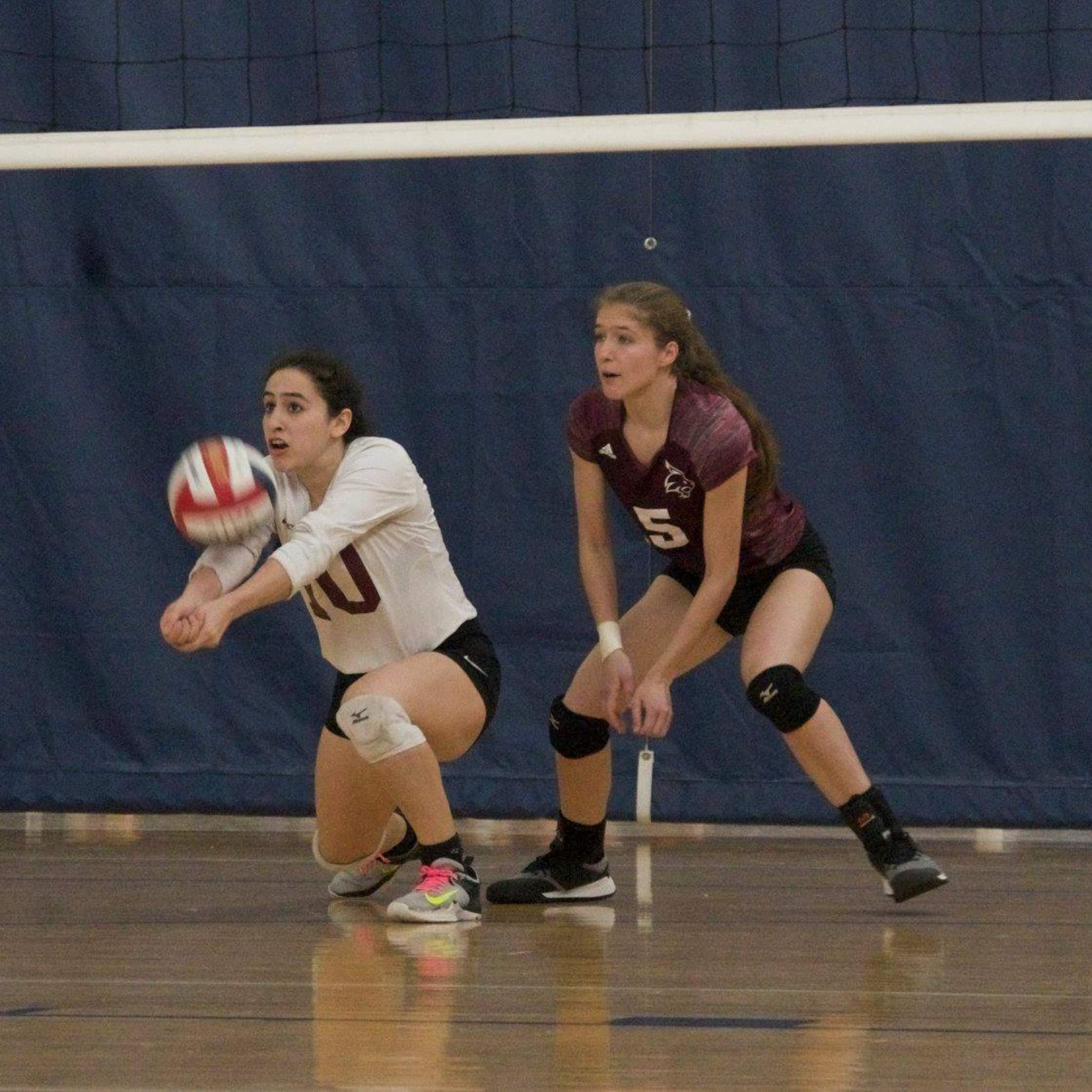Women's Volleyball player bumps ball up from one knee on court