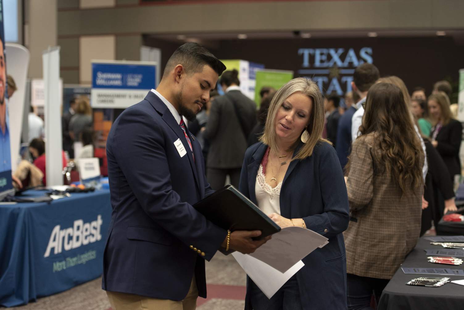 A student and a professional in discussion while looking over a folder of papers during a Career Fair in the LBJ ballroom