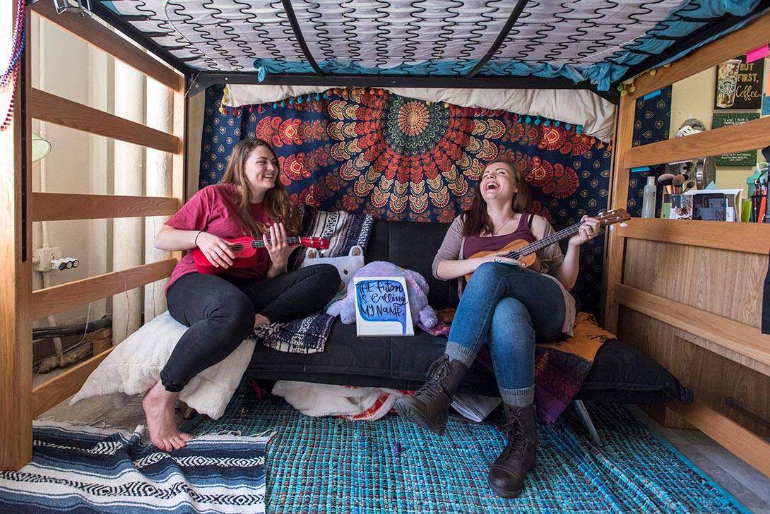 two female students lounge on the futon in their dorm room