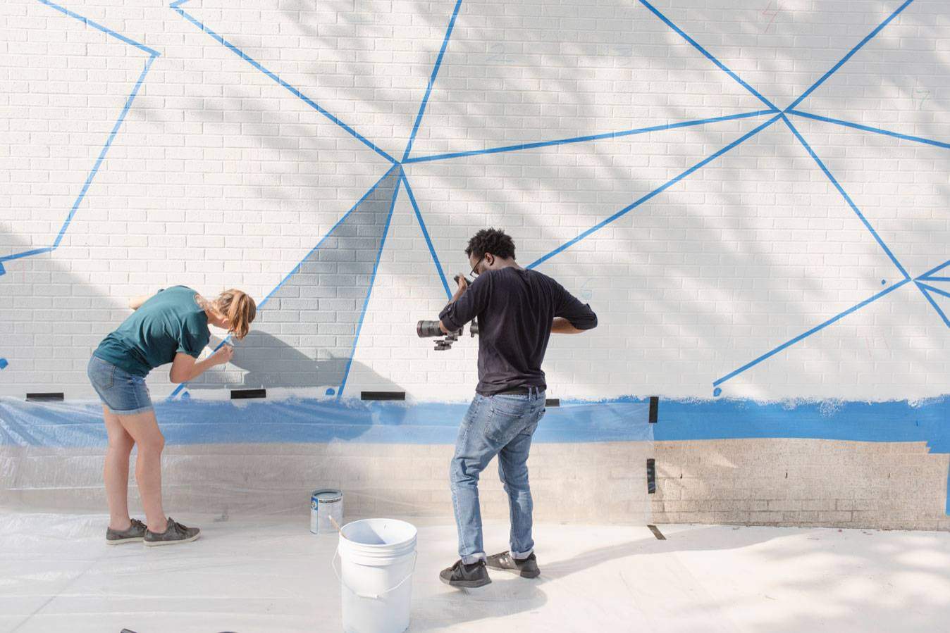A videographer filming an artist paint a mural