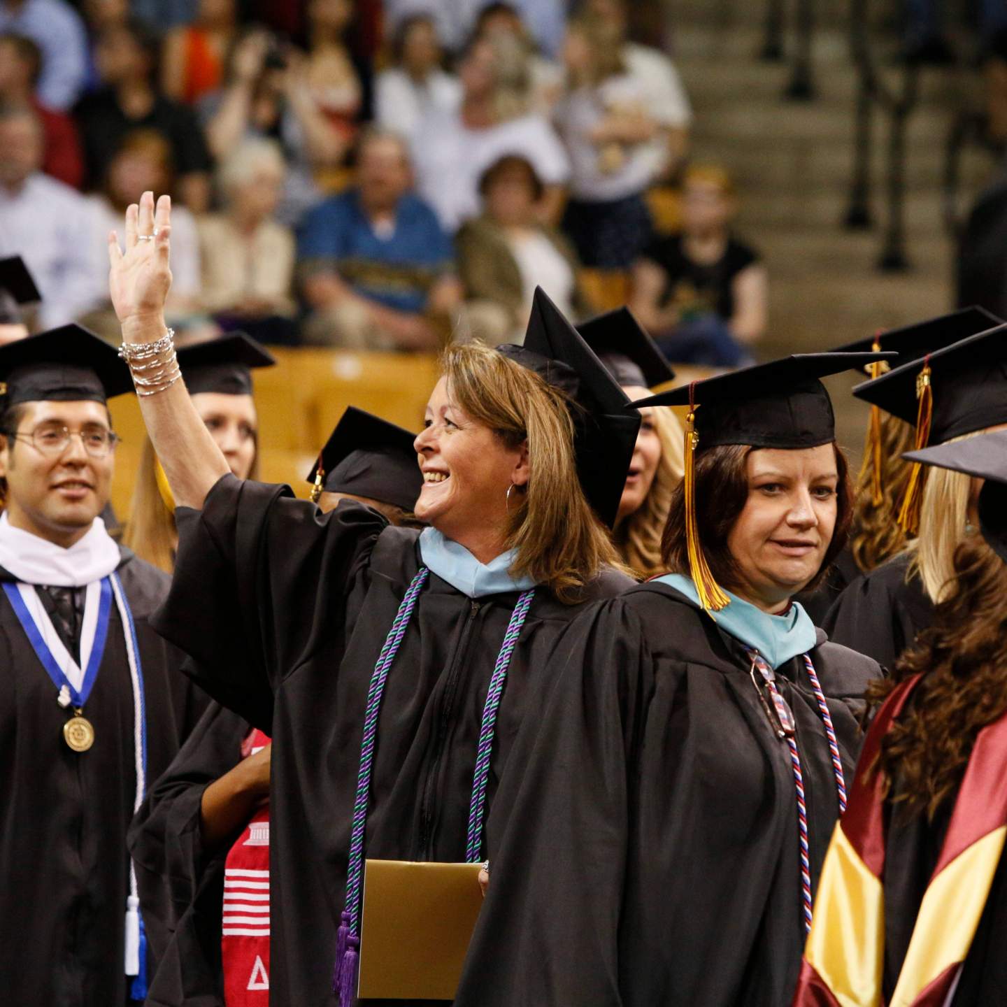 ae enthusiastic graduate waving to her guest during commencement ceremony