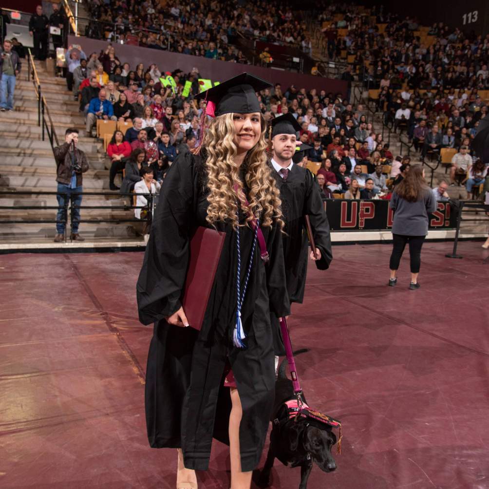 graduate holding diploma with service dog wearing a graduation cap