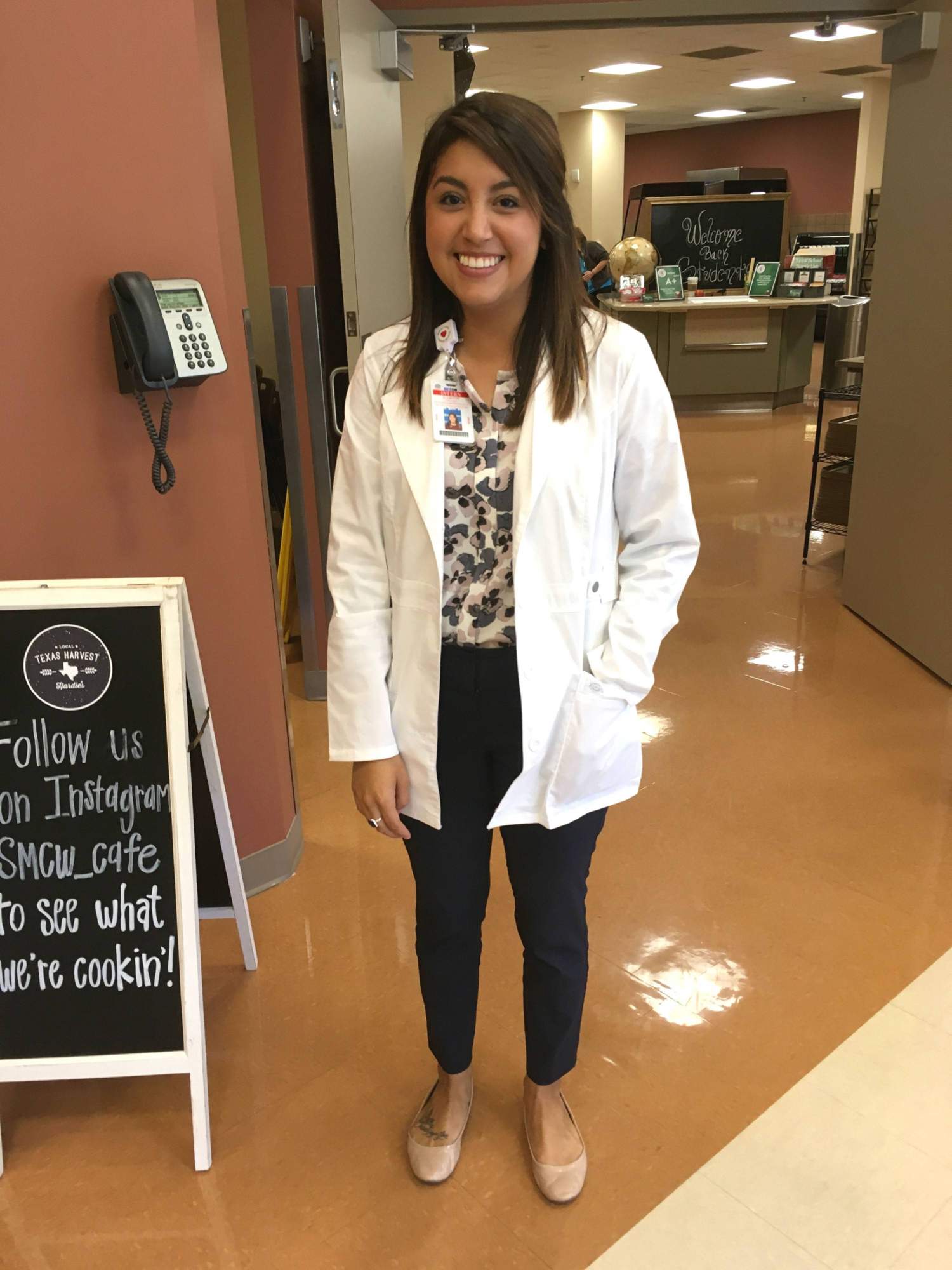 Latina woman in lab coat poses for picture in hsopital kitchen