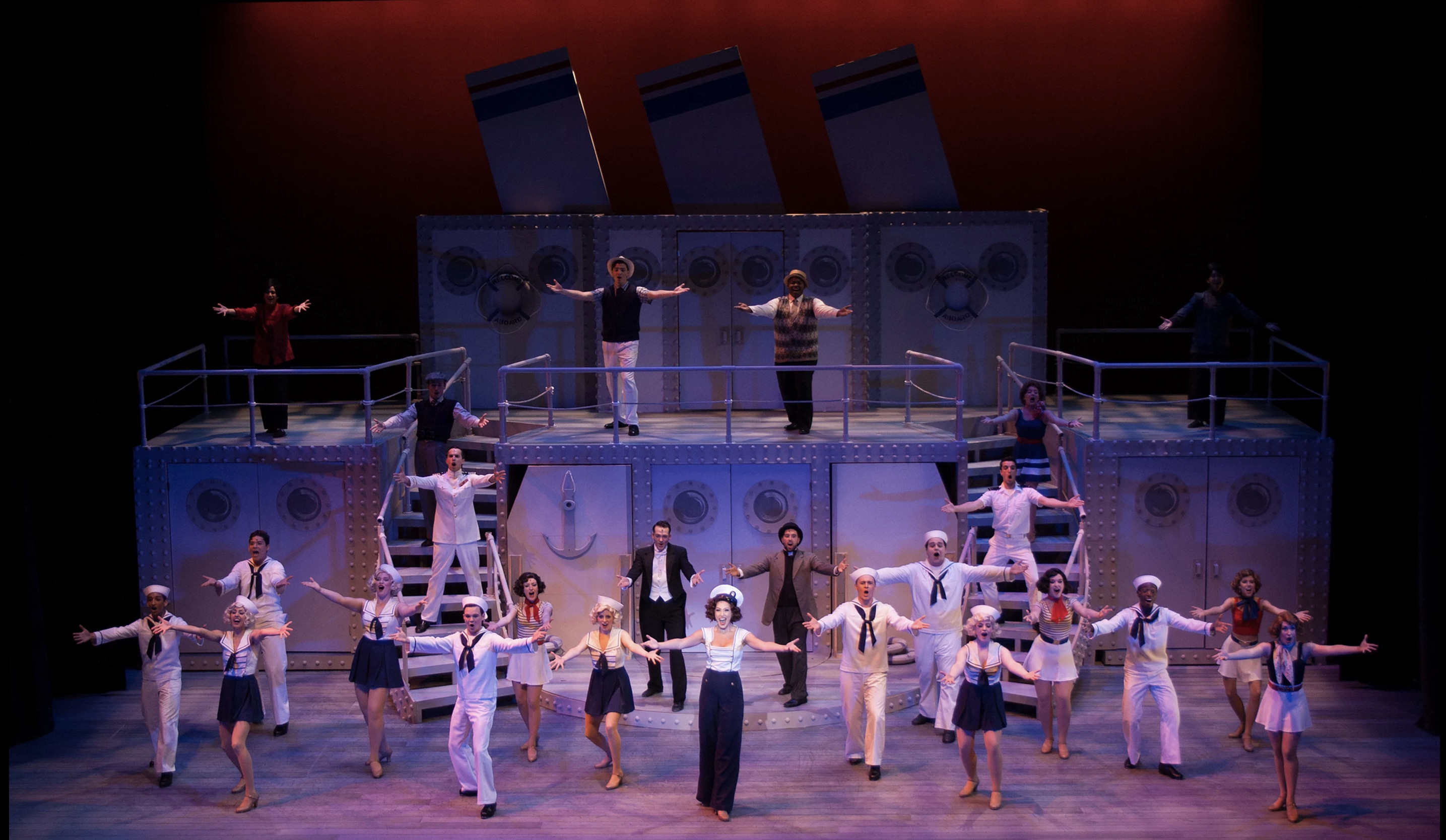 Full cast in sailor outfits on the cruise boat, striking a pose with their arms out. 