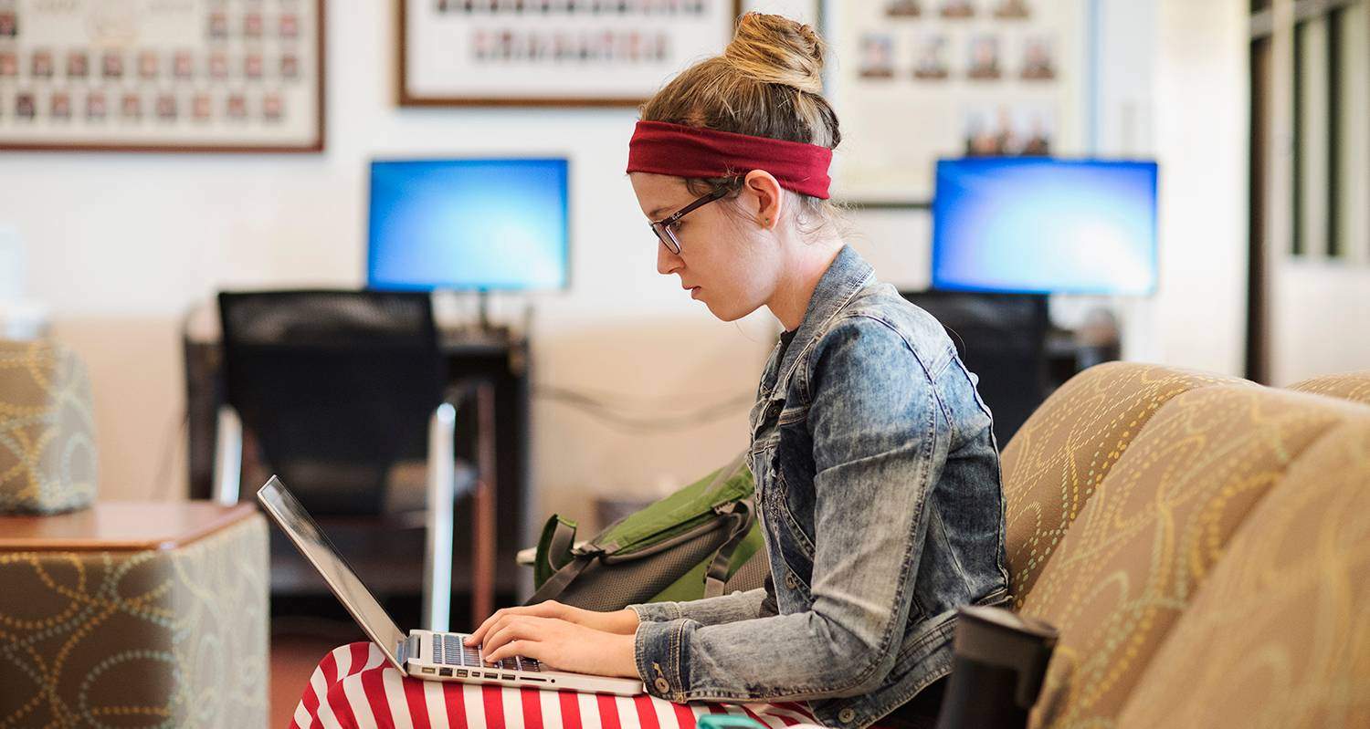 A student sits on a couch with her laptop