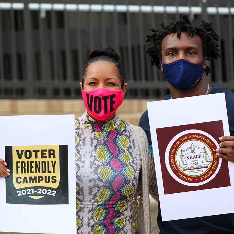 staff member and student holding signs