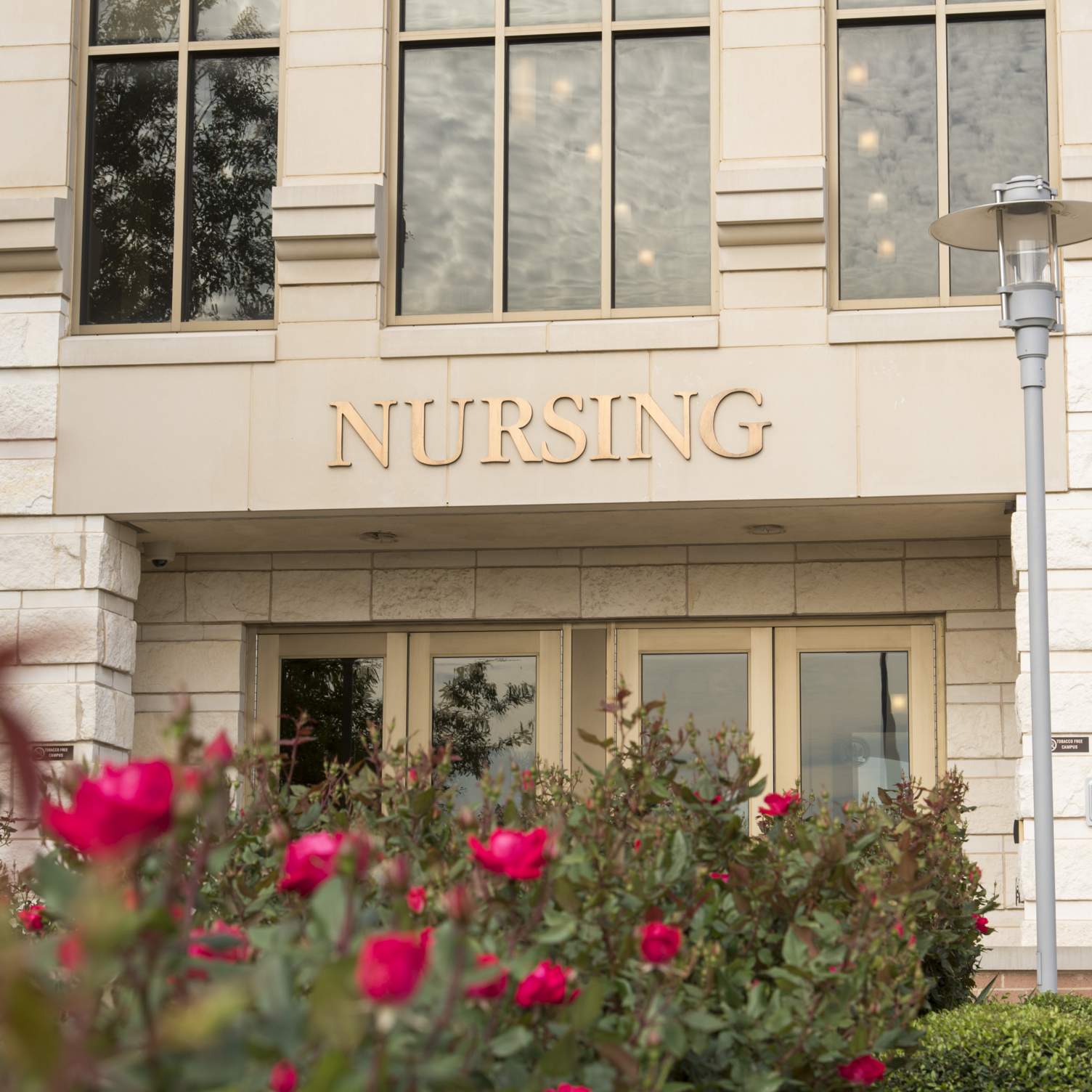 a close up of a round rock building that says "nursing" with red flowers in the landscaping