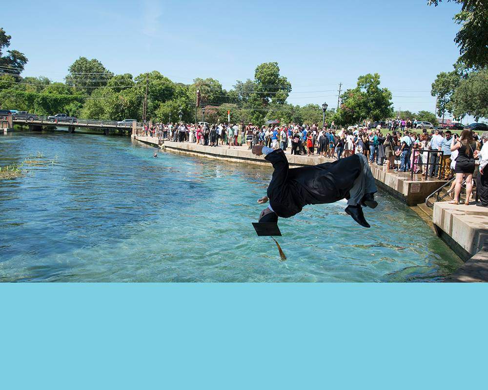 Graduate jumping in the crystal-clear San Marcos river with stripe of light blue color