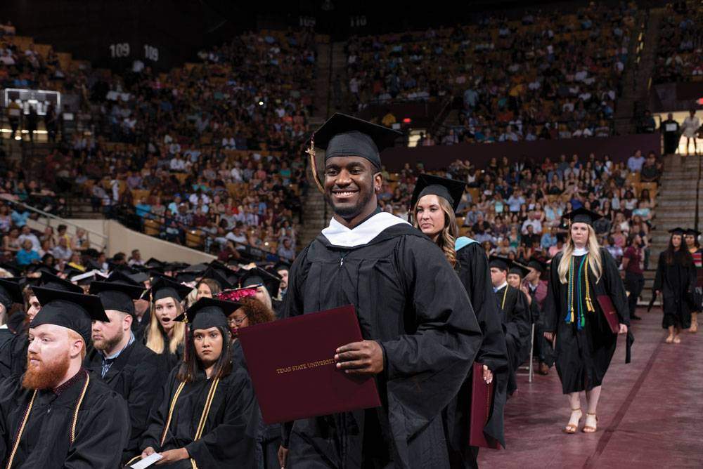 Photo of Texas State Graduate at graduation with his diploma.