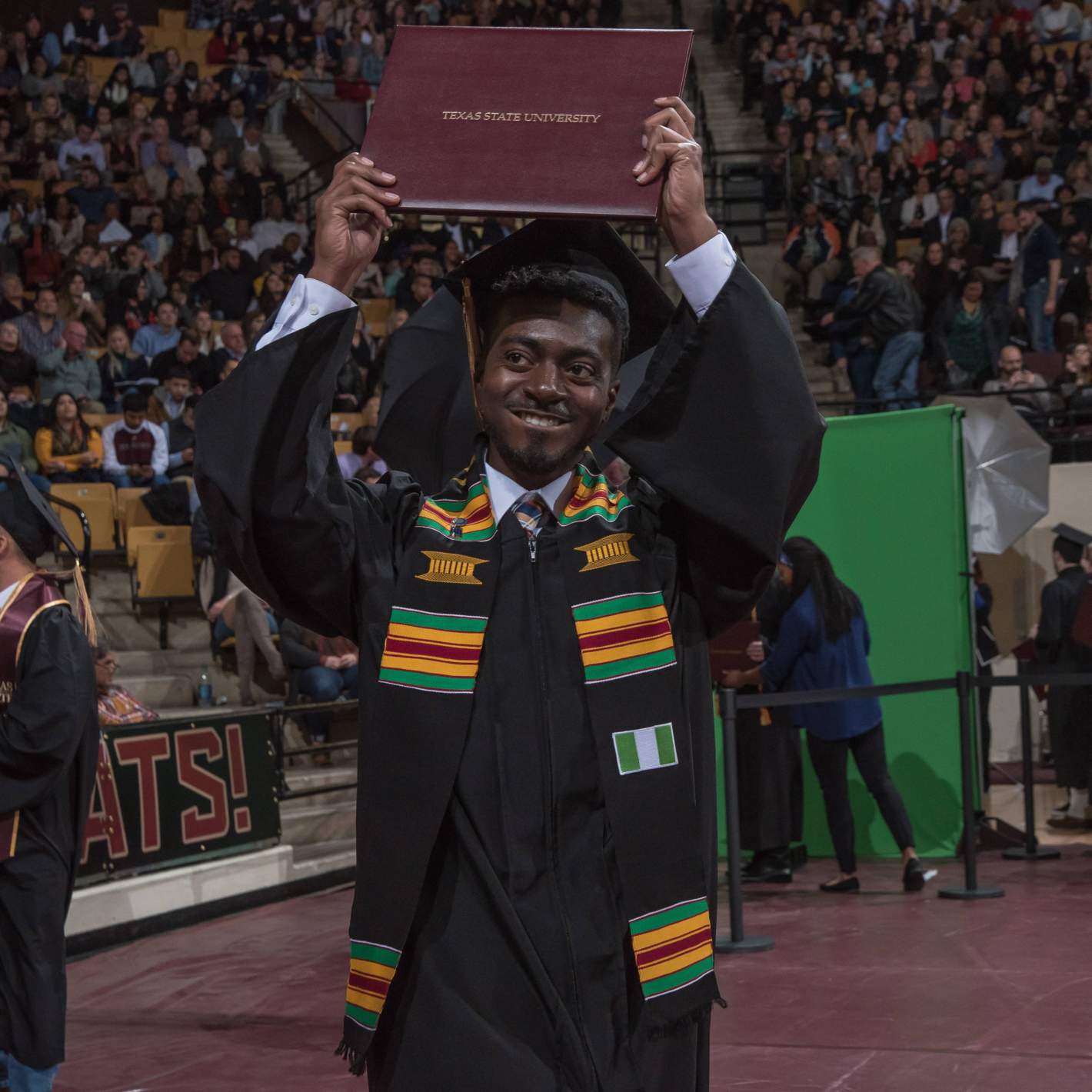 graduate smiling, holding diploma overhead