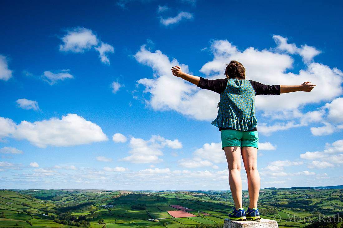 An image of a student, standing on a cliff's edge, overlooking a field in Wales.