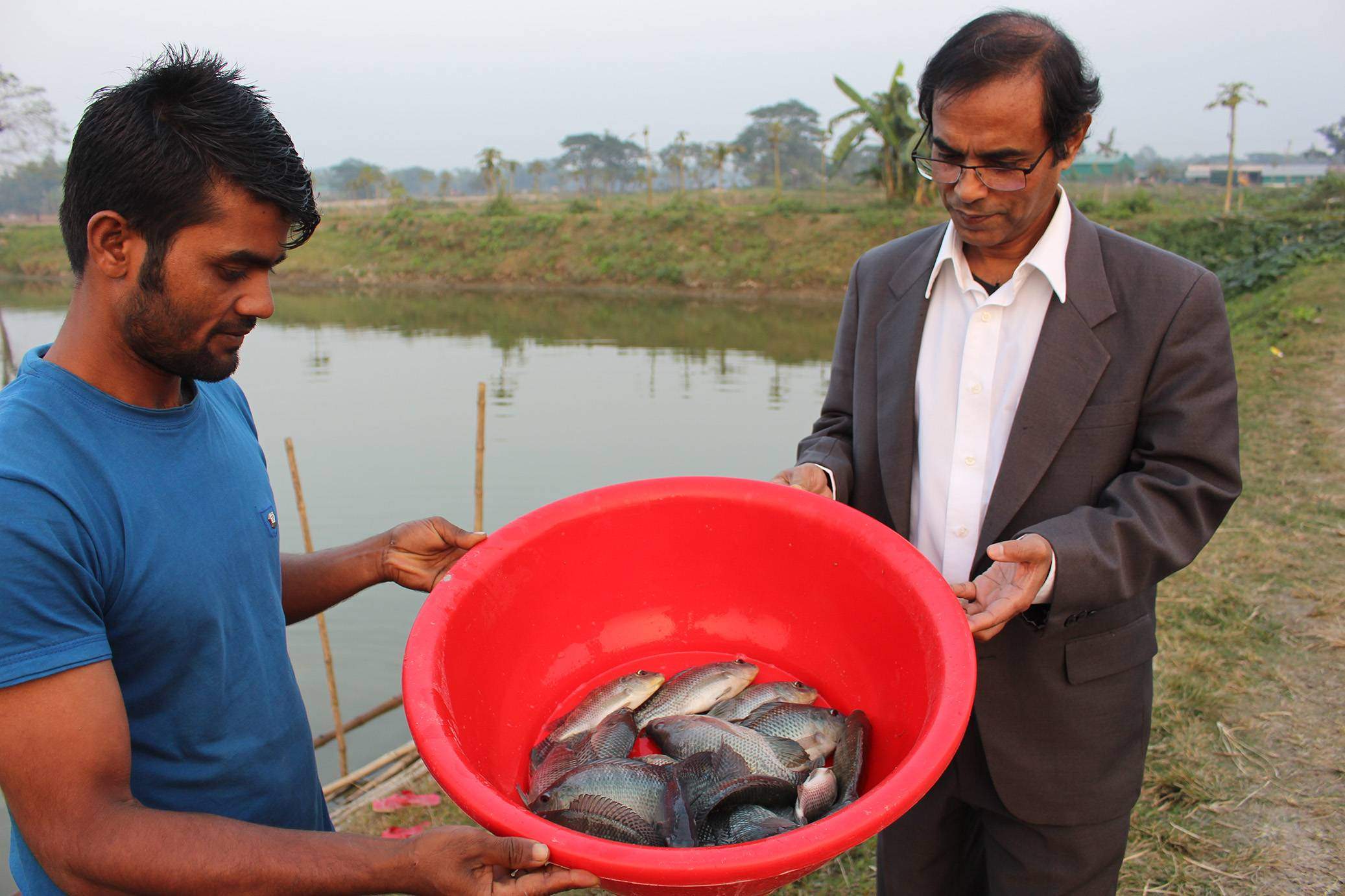 two men holding a bucket of fish