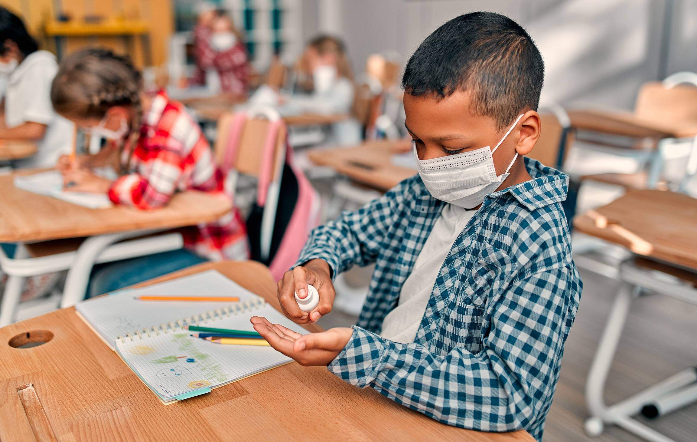 young student wearing mask in classroom using hand sanitizer