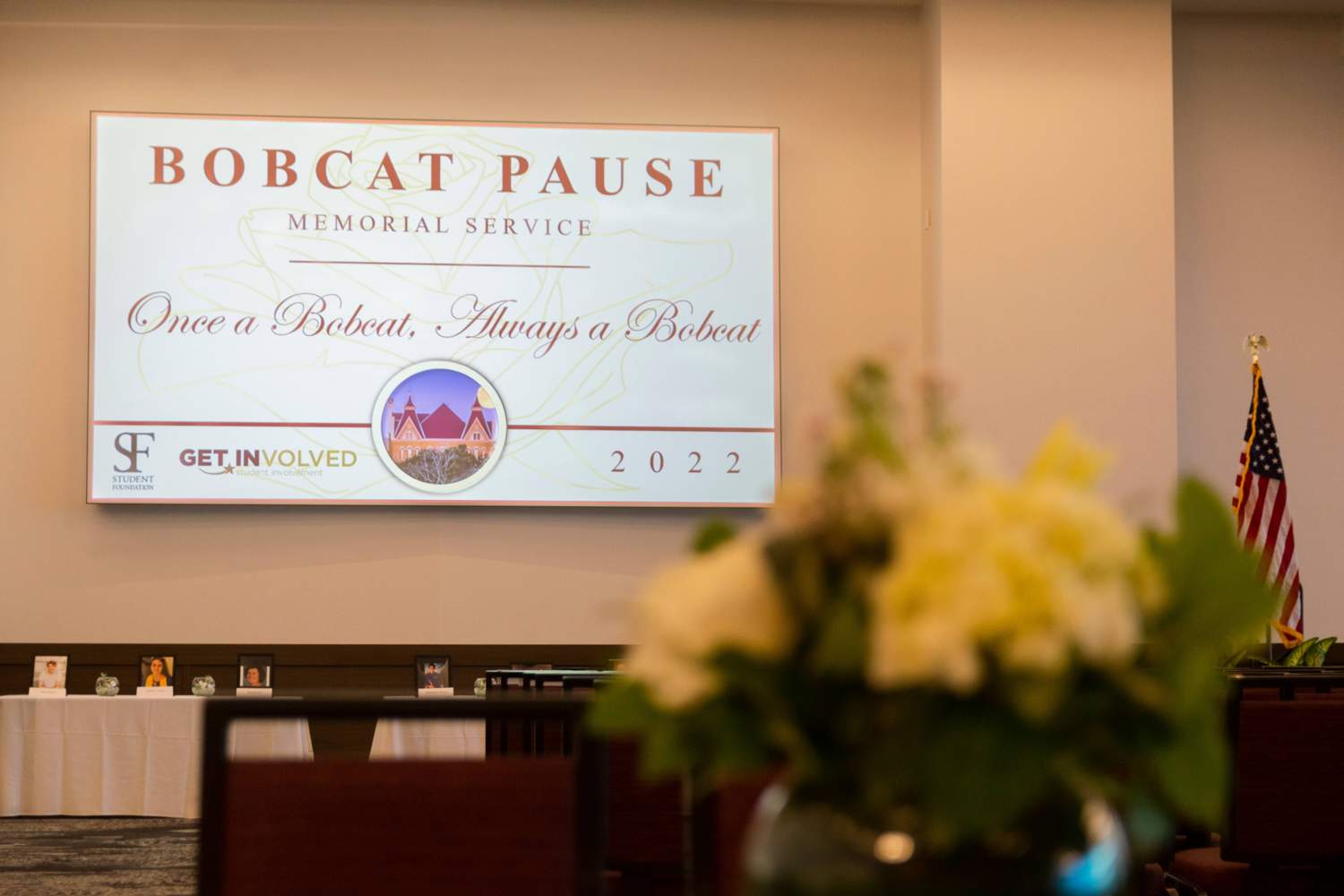 Photo of flowers in the foreground with screen presenting Bobcat Pause opening powerpoint slide in background