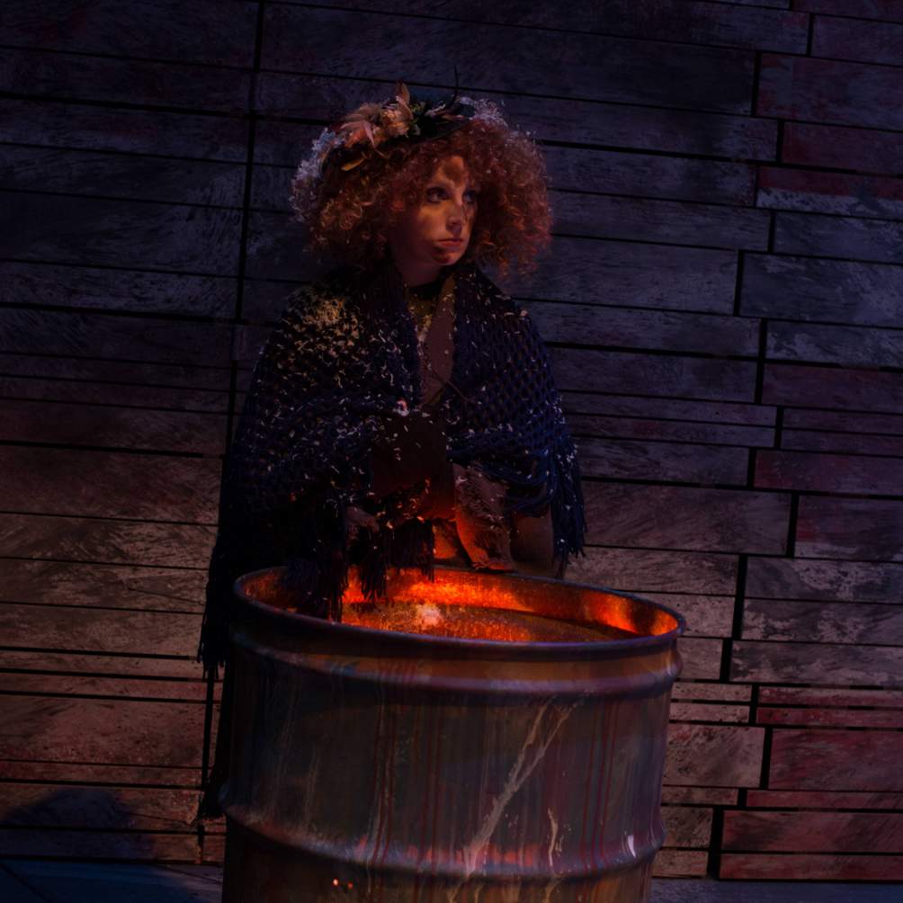 Beggar woman standing over a fire in a barrel 