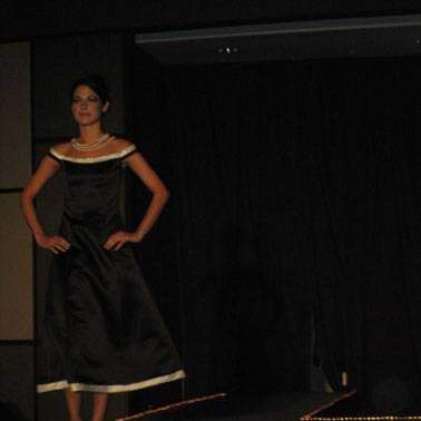 Student/model in black dress with white trim, wearing cute strap-sandals with high-heels,  walking down the runway. 