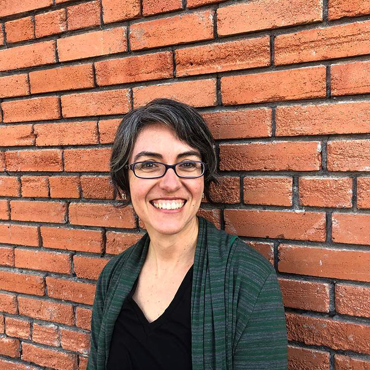 Dr. Anadelia Romo, Associate Professor in Department of History leaning against brick wall 
