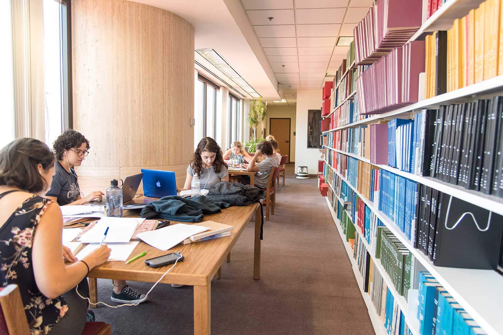 female students study at a table beside a colorful book shelf