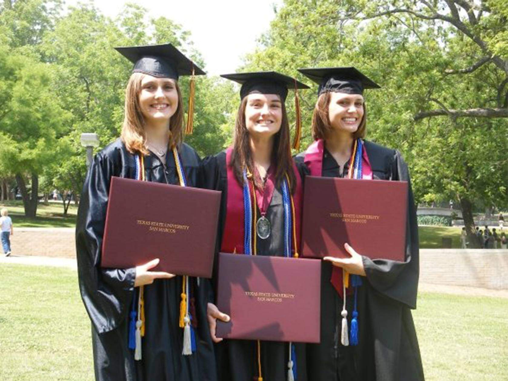 three graduates holding diplomas