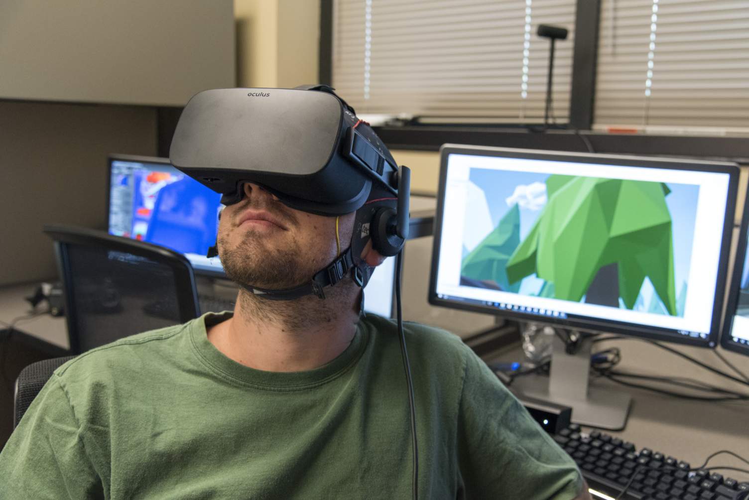 Male student seated with virtual reality goggles on face with computer sscreen in background