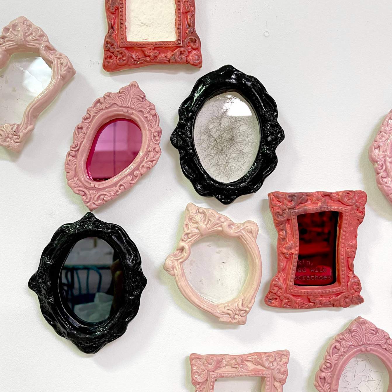 Student work: ceramic picture frames of various shapes encircling mirrors and installed in a group