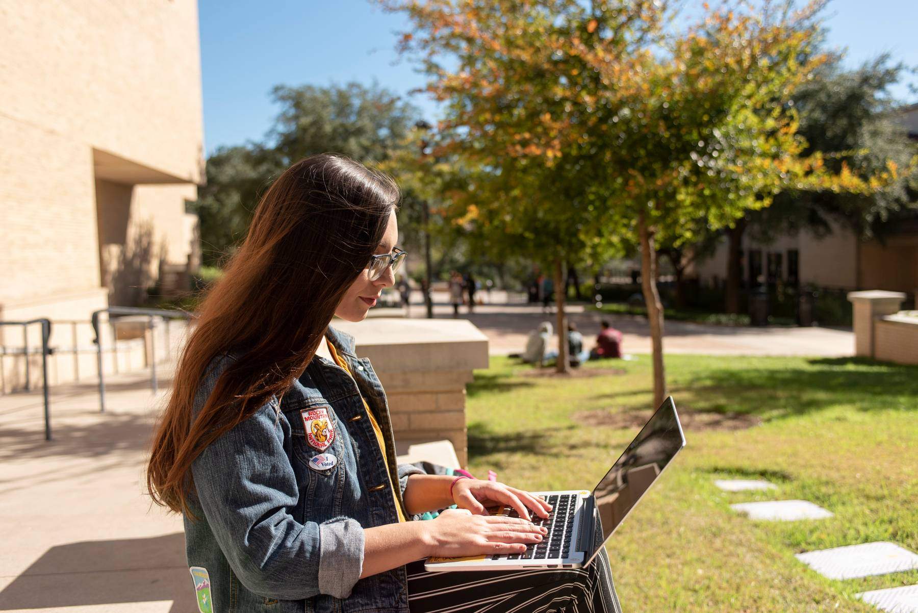 A student typing on a laptop outdoors.