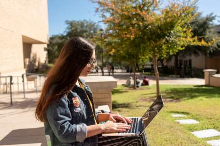 Student sits outside working on laptop on campus.