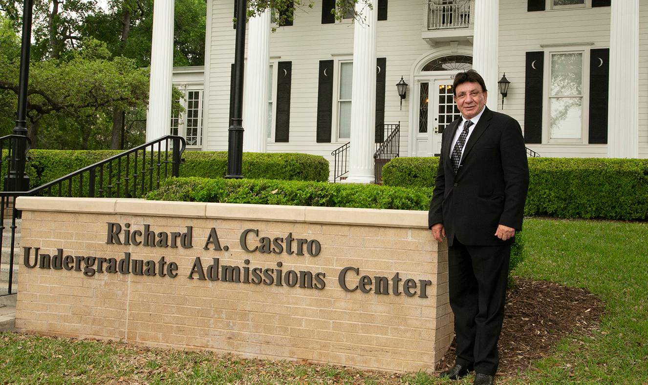 man in suit standing next to brick sign reading "Richard A. Castro Undergraduate Admissions Center"