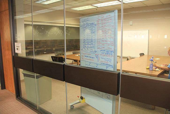 a view through a glass wall into a group study room with tables and white board