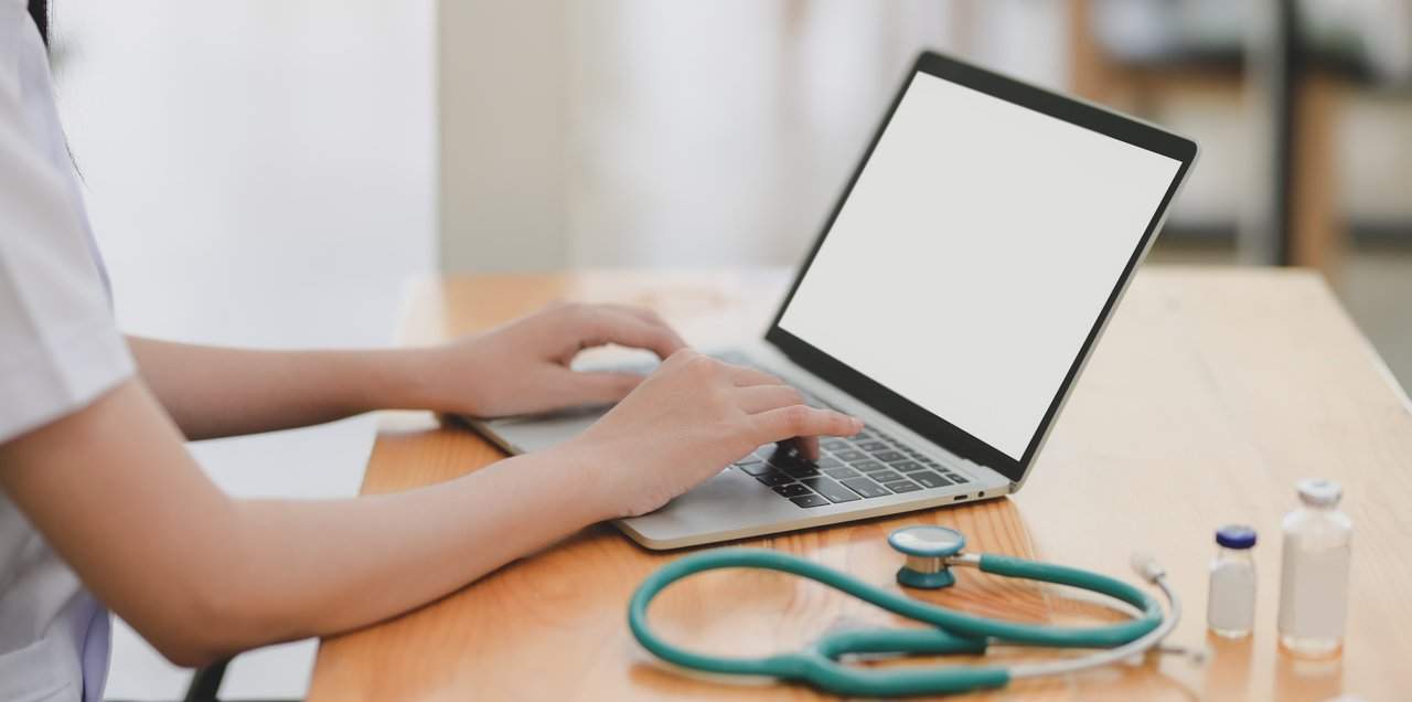 Woman sits infront of a laptop with a medical equiptment beside.
