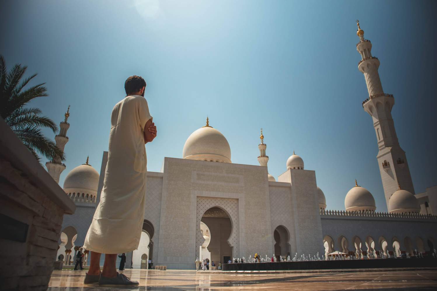 A wide shot of a person wearing white thawb standing at Sheikh Zayed Grand Mosque Center in Abu Dhabi by Artur Aldyrkhanov
