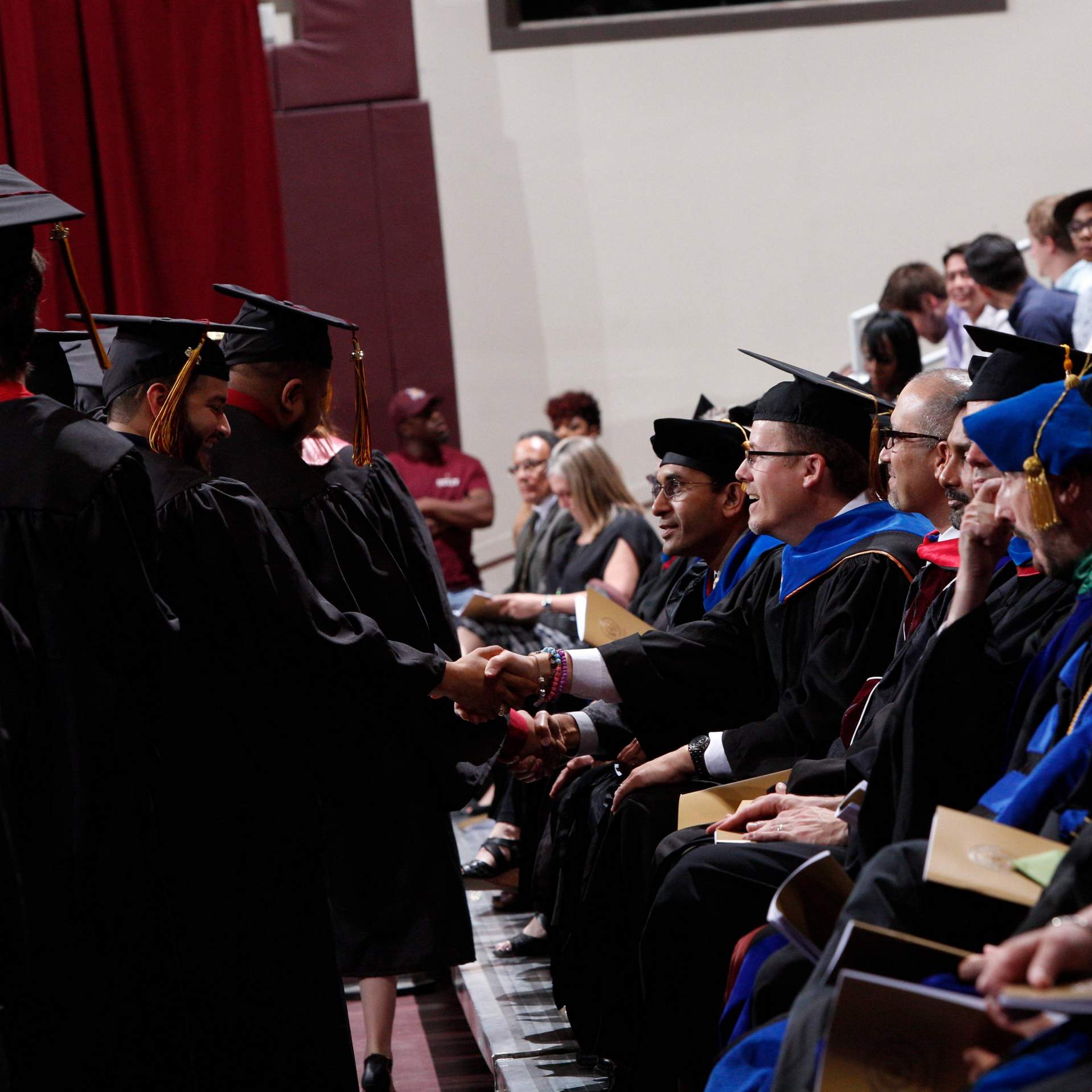Faculty members congratulate their graduating students as they line up to receive their diploma and shake hands with the President of Texas State University at a Spring 2016 commencement ceremony.