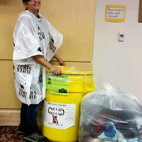 Texas State University Student Angel Caraveo dons a Bobcat poncho as she collects student donations during this week’s stormy weather for the university’s “green” move-out program. Pack It Up and Pass It On collects more than seven tons of student donations such as clothing, shoes, office supplies, and small electronics that are “reused” by local low-income residents who “shop” from among the donations. 