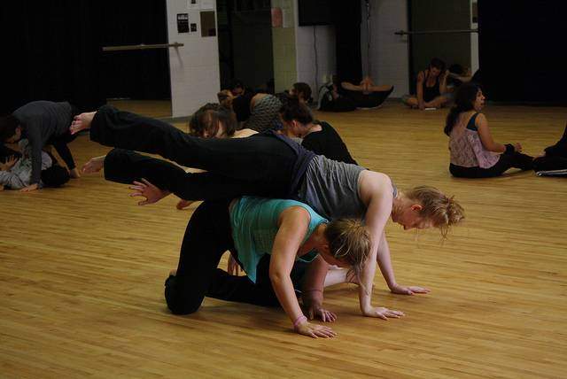 two dancers, one student kneeling on the ground, the other laying across them. 