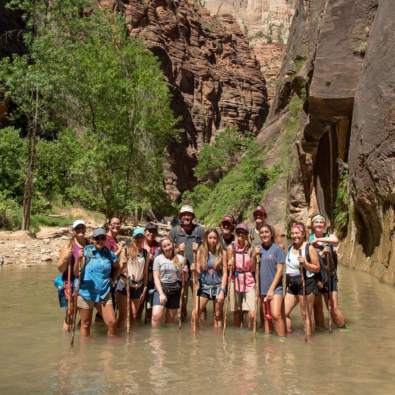 A class full of students and their professor pose in a shallow river