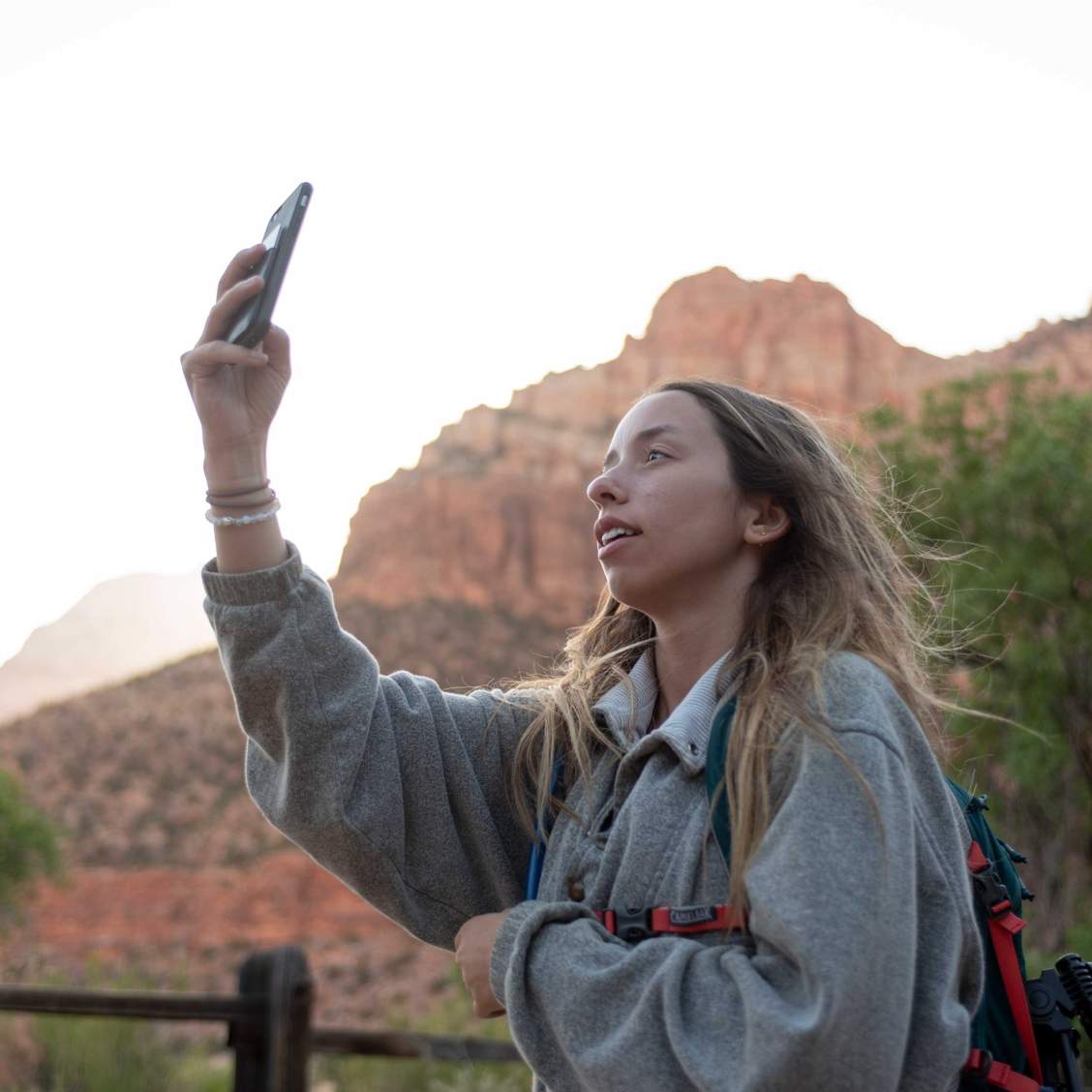 A student holds her phone up, surrounded by mountains