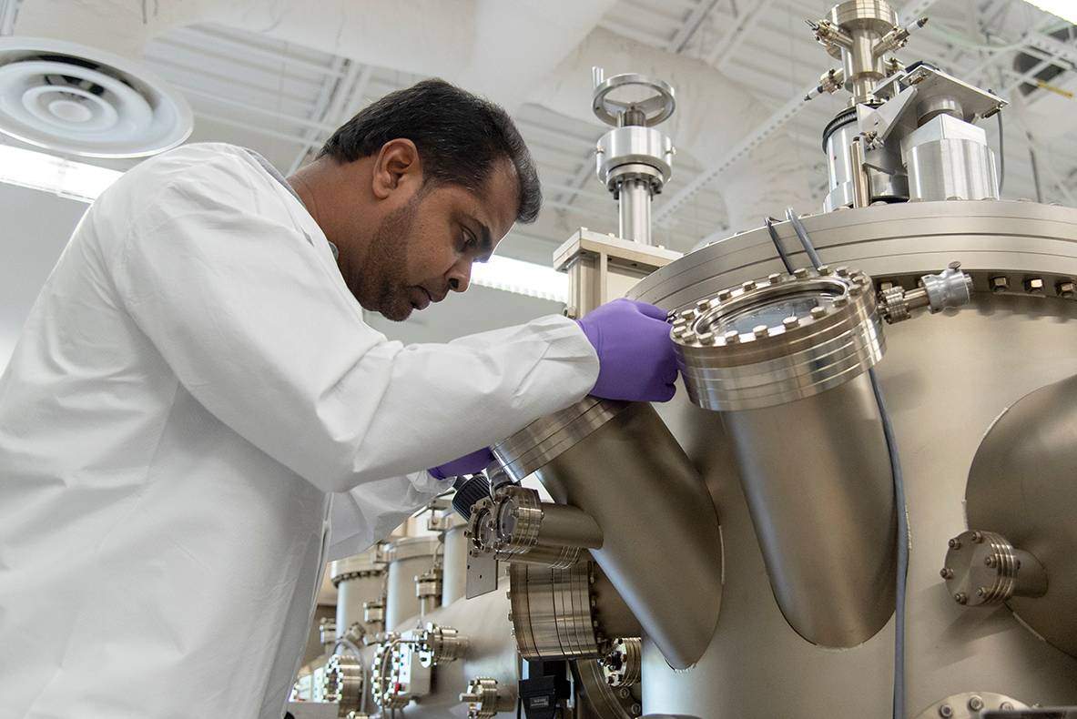 man in white lab coat looking into large metal container