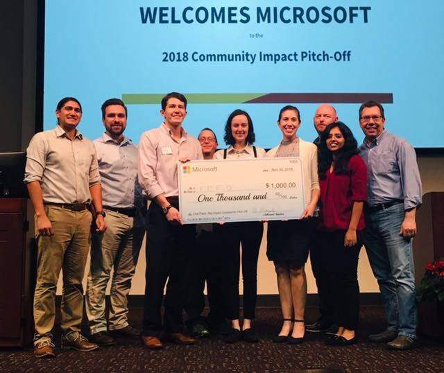 students holding a check in front of a sign "2018 Community Impact Pitch-off"