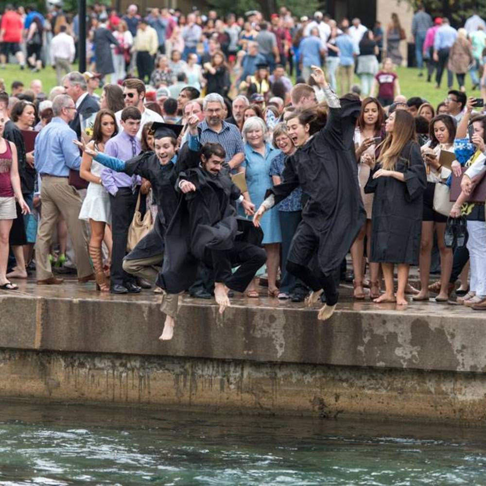 crowd taking photos as graduates jump into the river